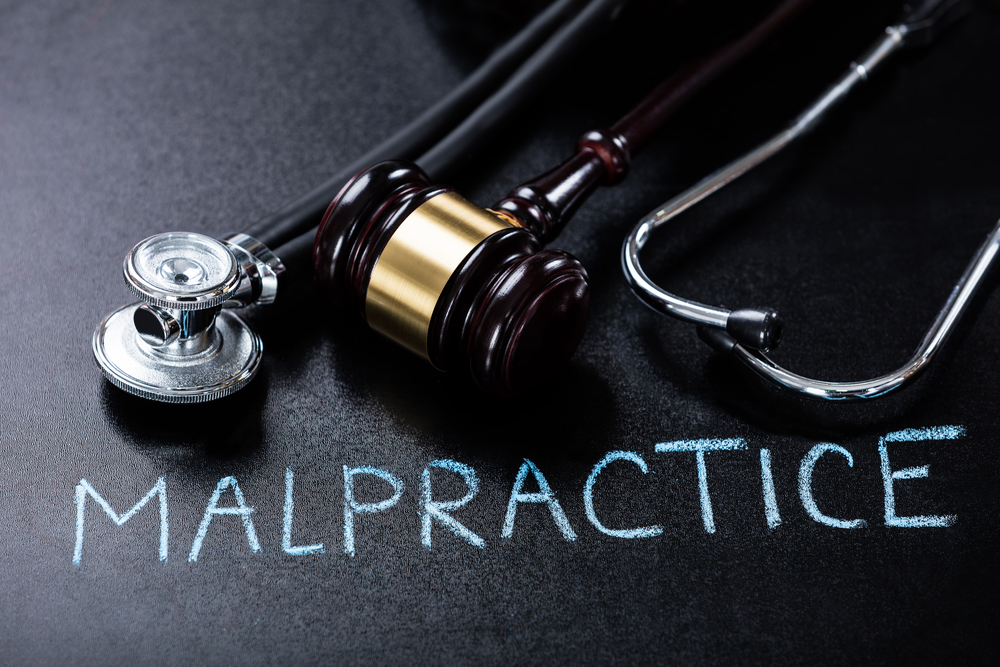 "Malpractice" written on a table with a stethoscope and gavel next to it